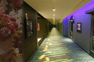A hotel corridor with a carpeted floor, framed pictures on the walls, and a purple-lit ceiling.