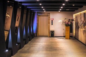 Hotellin käytävä, jossa on puulattia, vastaanottotiski ja seinälle asennettu valokuvien esittelyseinä.