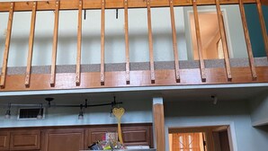 Ein Zimmer mit Deckenventilator, Holzgeländer, einer Küchenzeile mit Schränken und einem Wäschekorb.