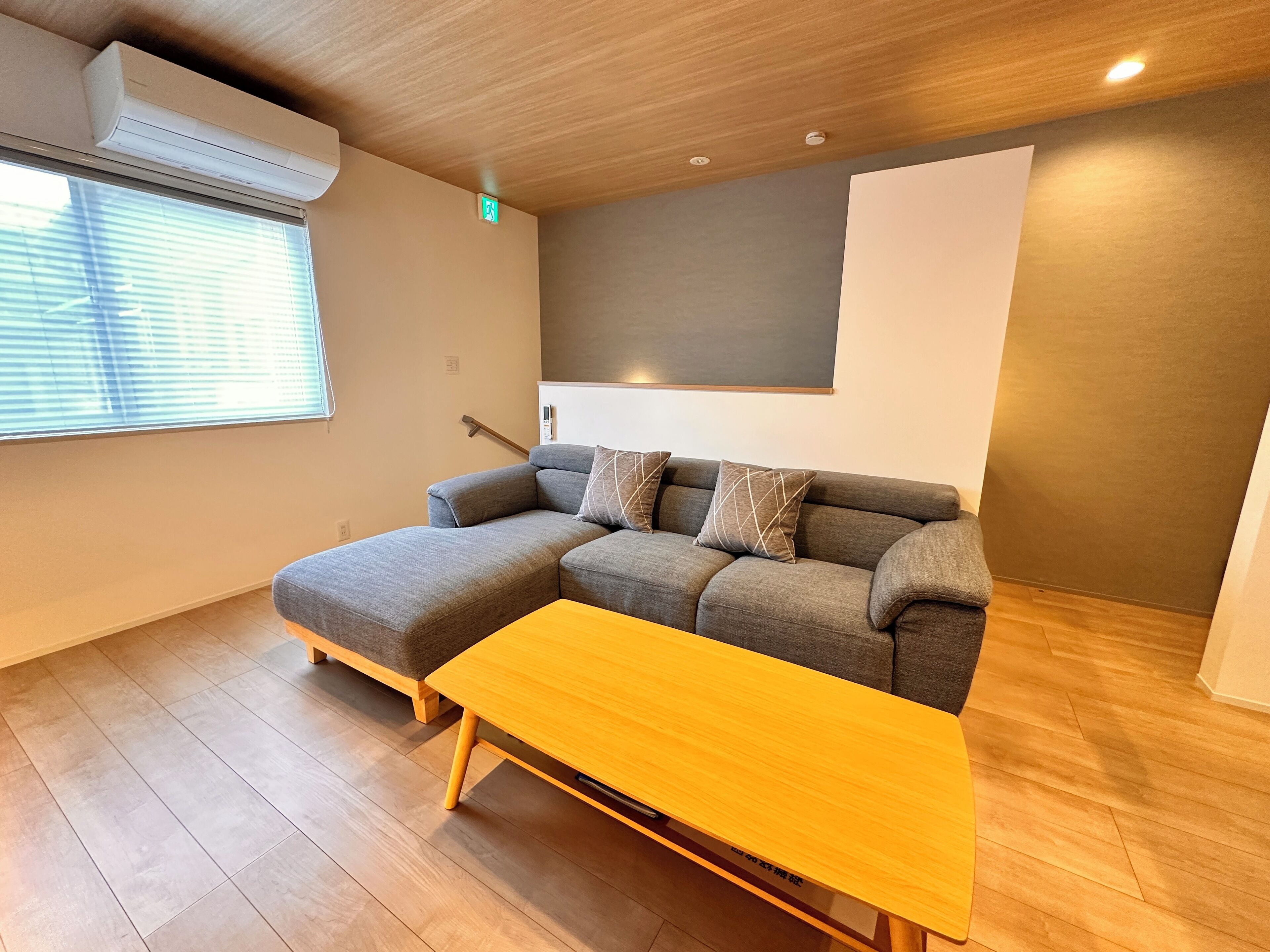 A modern living room with a sectional sofa, a wooden coffee table, and an air conditioning unit.