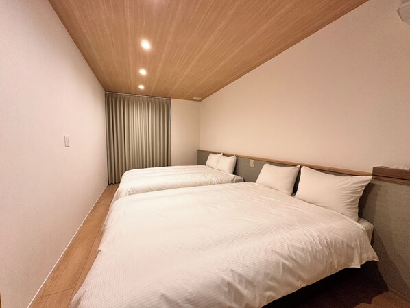 Quarto de hotel com duas camas, teto de madeira e cortina.