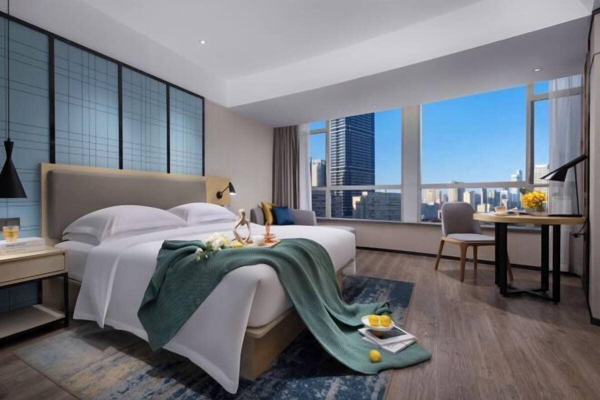 A modern hotel room with a large bed, a desk, and a view of the city skyline.