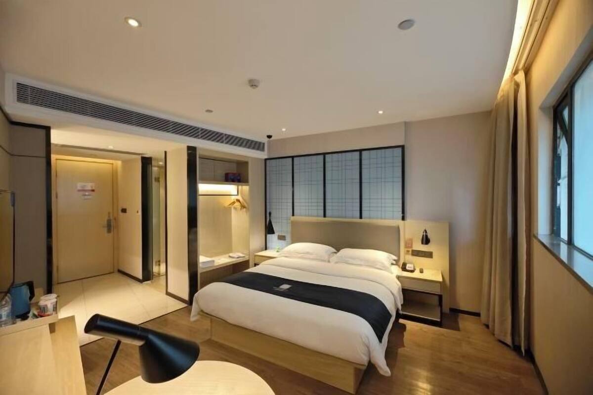 A modern hotel room with a large bed, bedside tables, a desk, and a window.