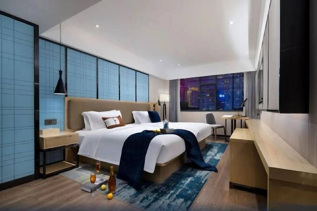 A modern hotel room with two beds, a desk, and a view of the cityscape.