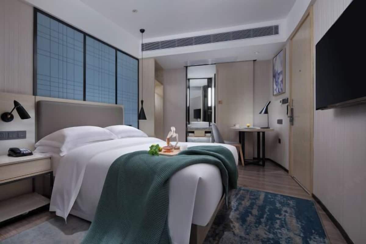 A hotel room with a bed, bedside table, lamp, and a desk with a chair.
