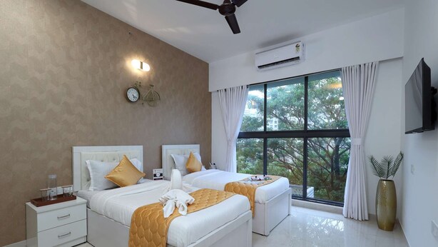 A modern hotel room with two beds, a large window with a view, a ceiling fan, and an air conditioning unit. - 3 BHK Urban Suite ( Gagal Home) (Mumbai)