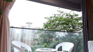 A balcony with two white wicker chairs and a small table, overlooking a cityscape with buildings and trees. - 3 BHK Urban Suite ( Gagal Home) (Mumbai)