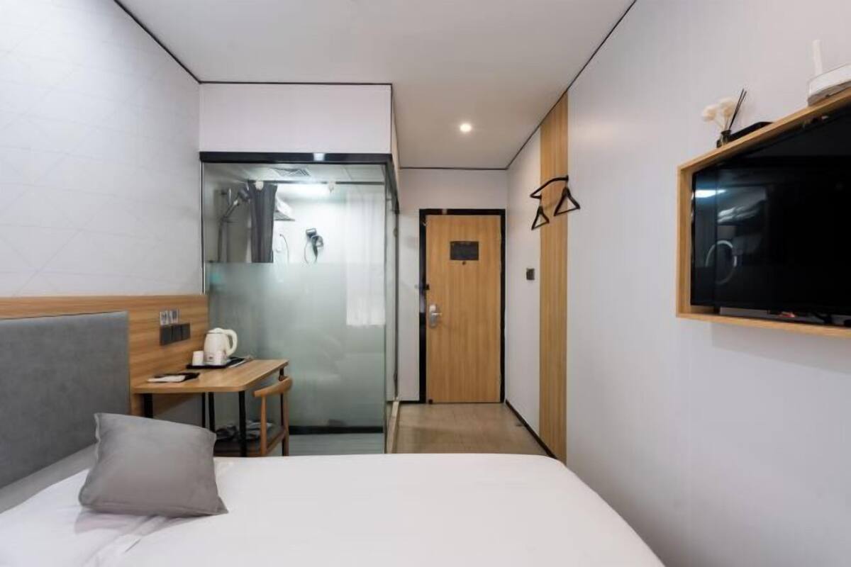 A hotel room with a bed, a desk, a television, and a shower area.