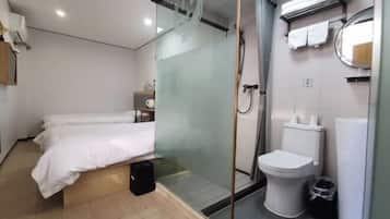 Ein modernes Hotelzimmer mit Bett, einer Duschkabine aus Glas, Toilette und einem kleinen Nachttisch mit Lampe.