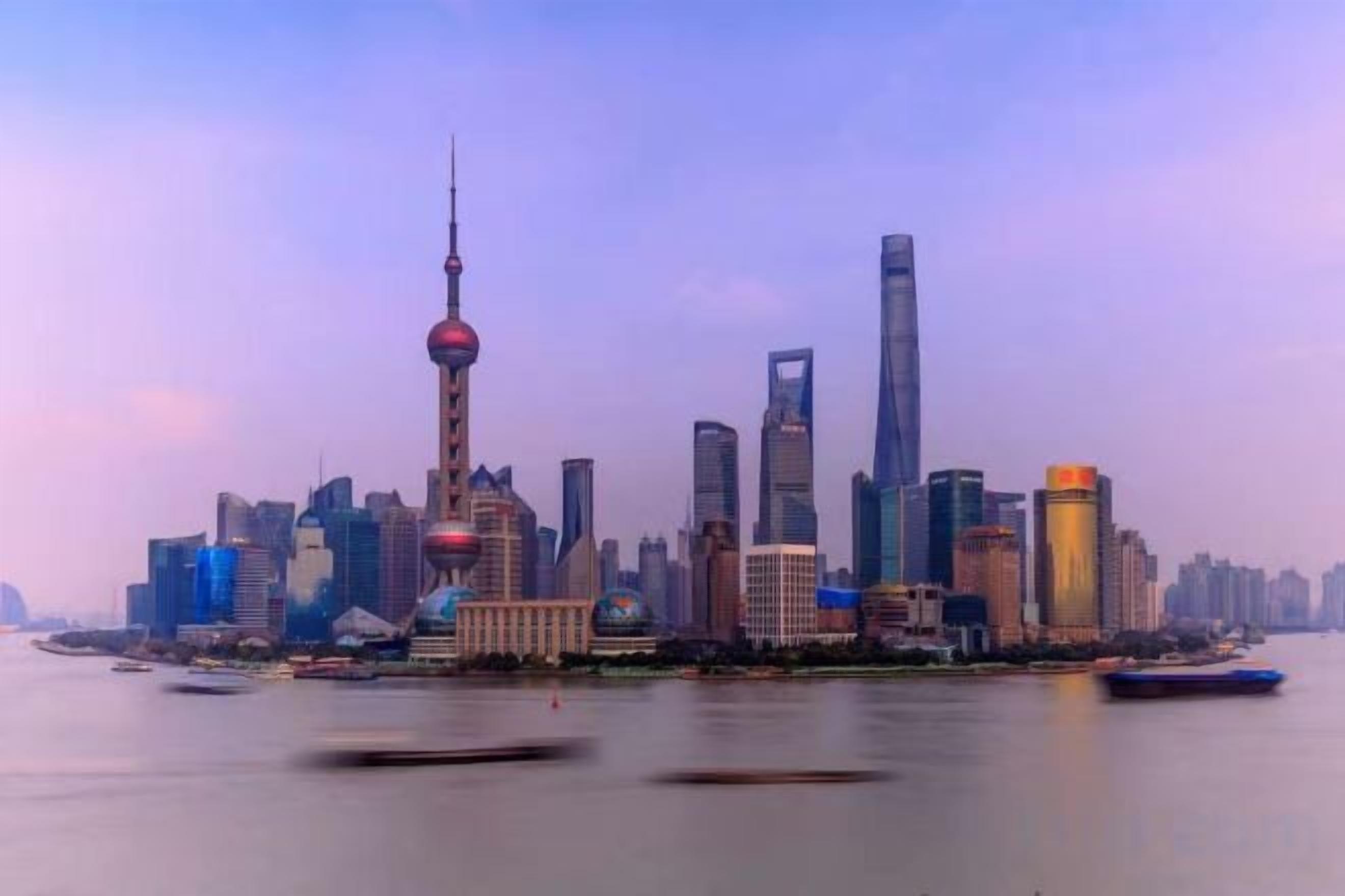 A city skyline with modern buildings, a prominent tower, and a body of water with boats.