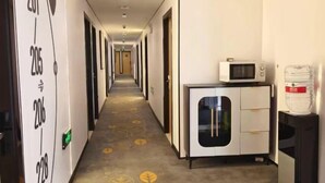 Pasillo de hotel con puertas numeradas, una kitchenette con microondas y un dispensador de agua.