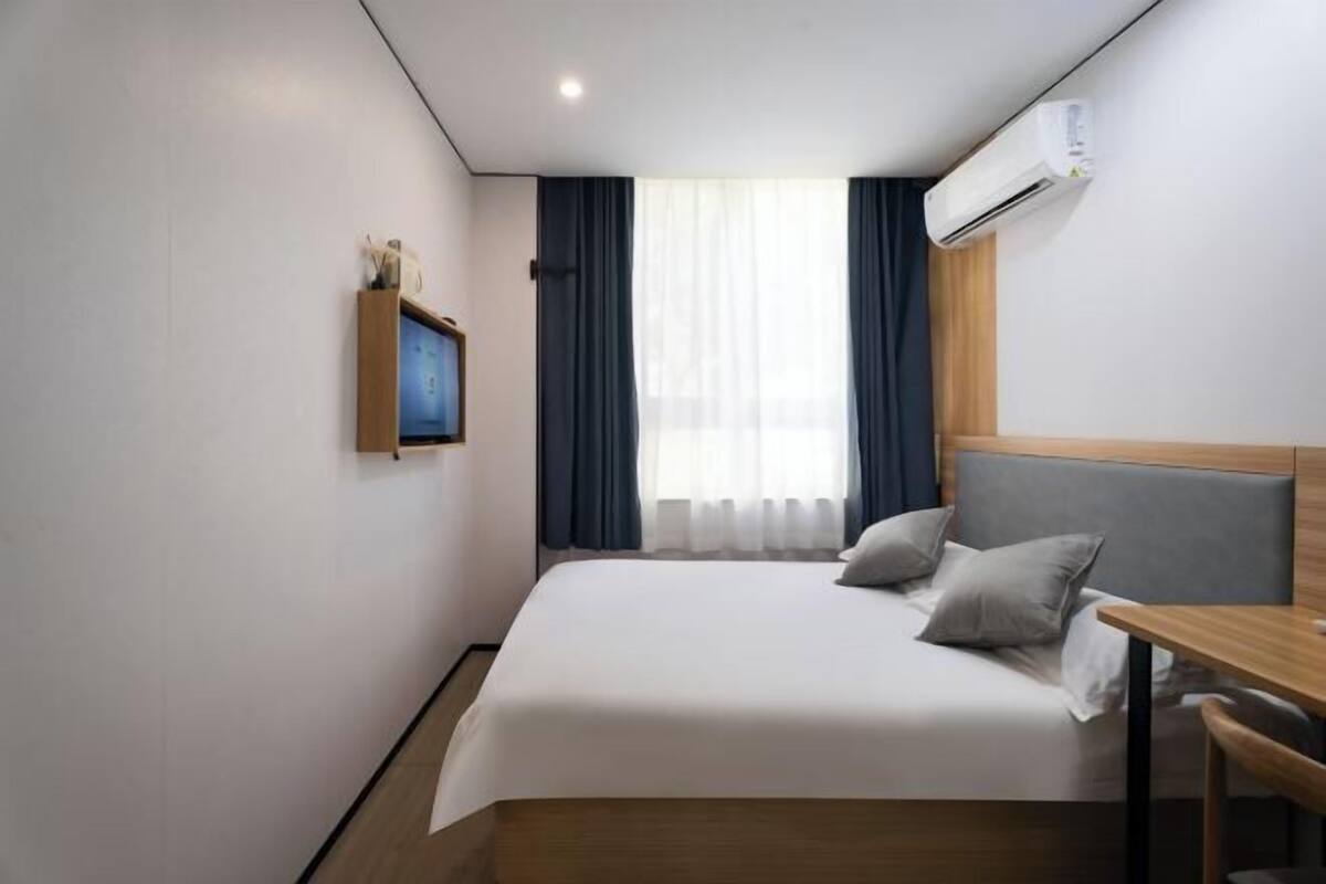 A compact hotel room with a single bed, a small desk, and a window with curtains.
