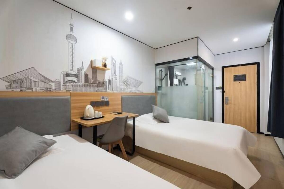 A hotel room with two beds, a desk, a chair, and a glass partition.