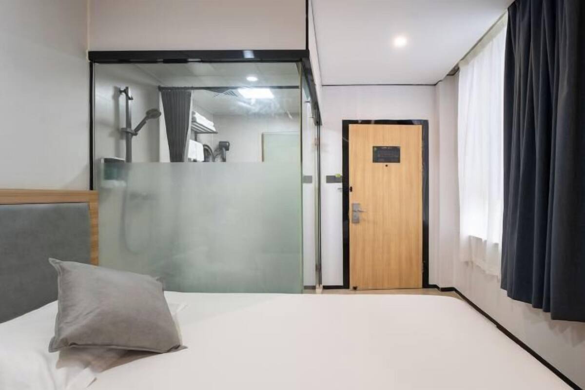 A hotel room with a bed, a wooden door, and a view of a bathroom through a frosted glass partition.