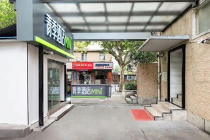 Una entrada de edificio con un corredor techado, un letrero de tienda y una escalera visible.