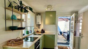 Una cocina compacta con pileta, estufa y muebles verdes. Hay una ventana que proporciona luz natural y vista al exterior.