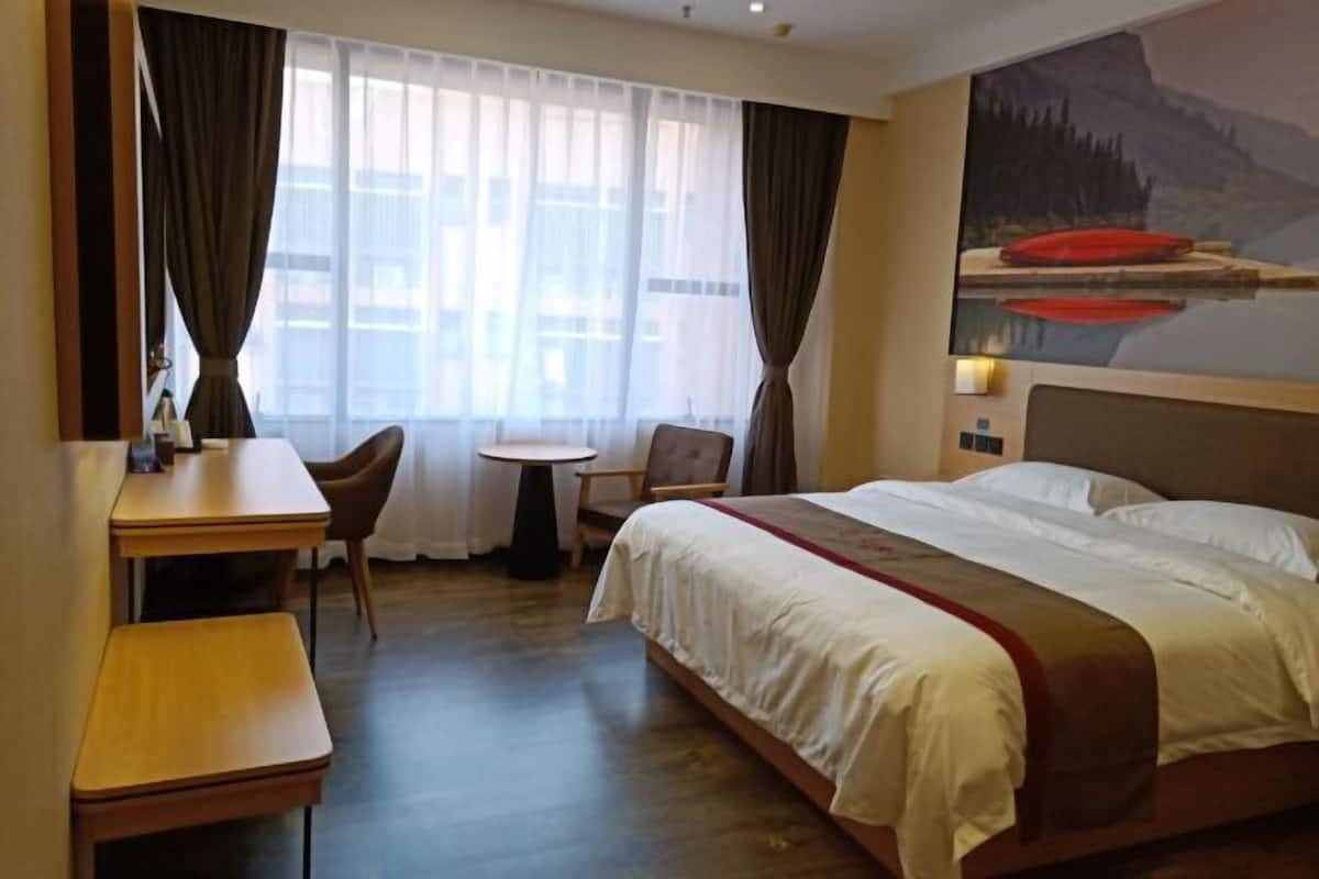 Una camera d'albergo con un letto, una scrivania, una sedia, un tavolino e un quadro appeso al muro.