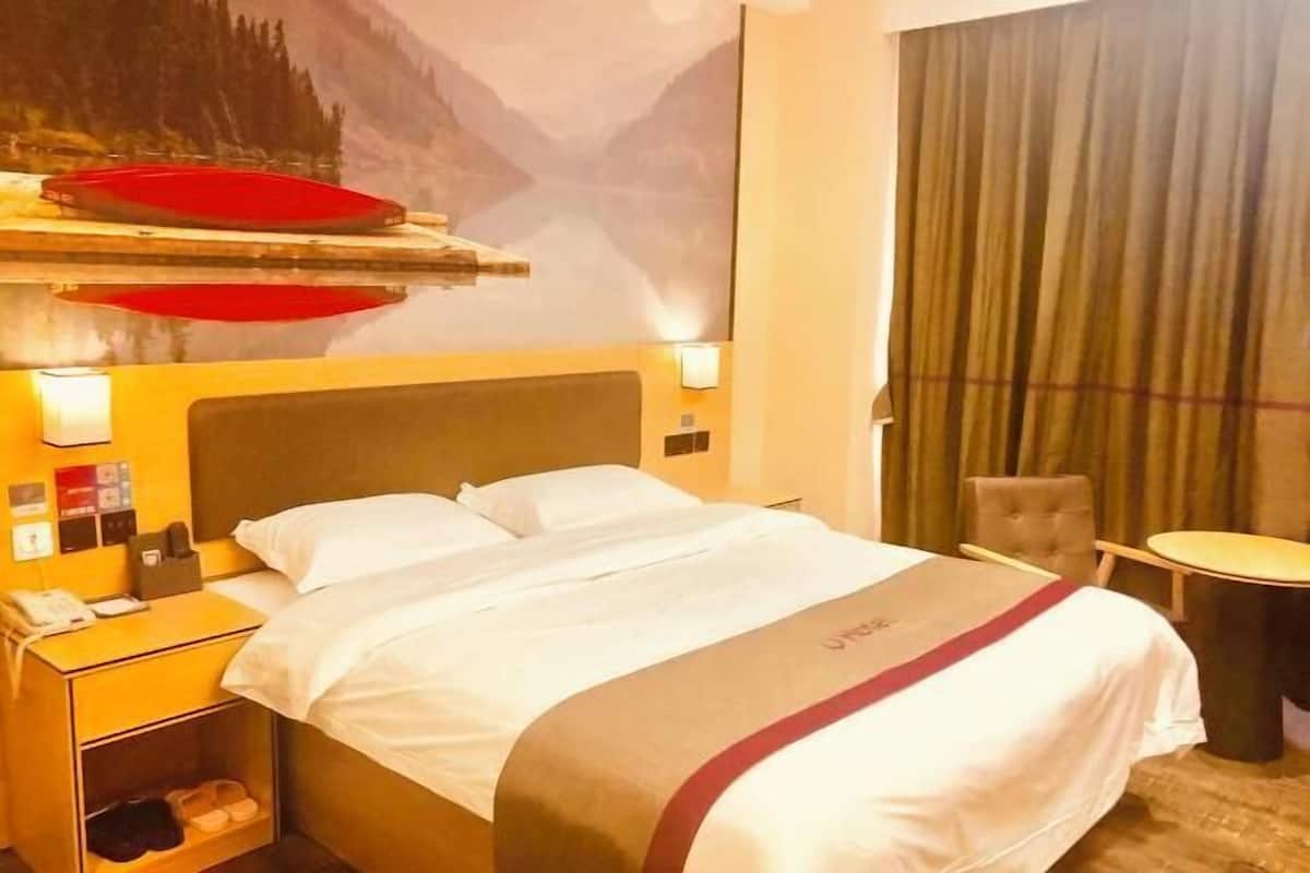 Camera d'albergo con un letto, un comodino, una lampada e una mensola a parete con un oggetto rosso.