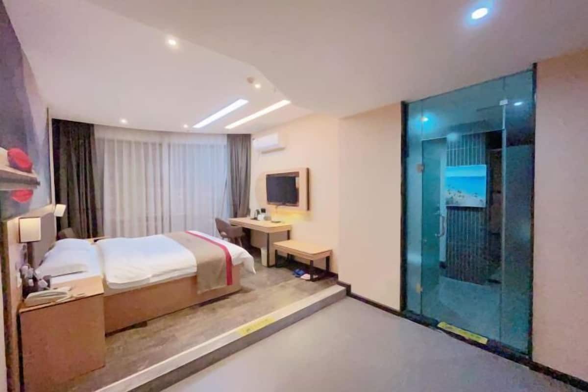 Camera d'albergo con un letto, una scrivania, una sedia, un televisore e la porta di un ascensore in vetro.