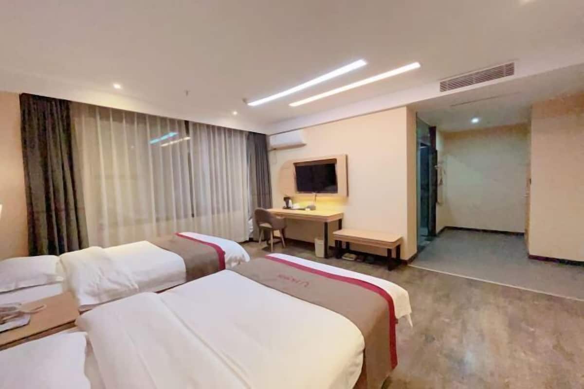 Camera d'albergo con due letti, una scrivania, una sedia, una TV e un'ampia finestra con tende.