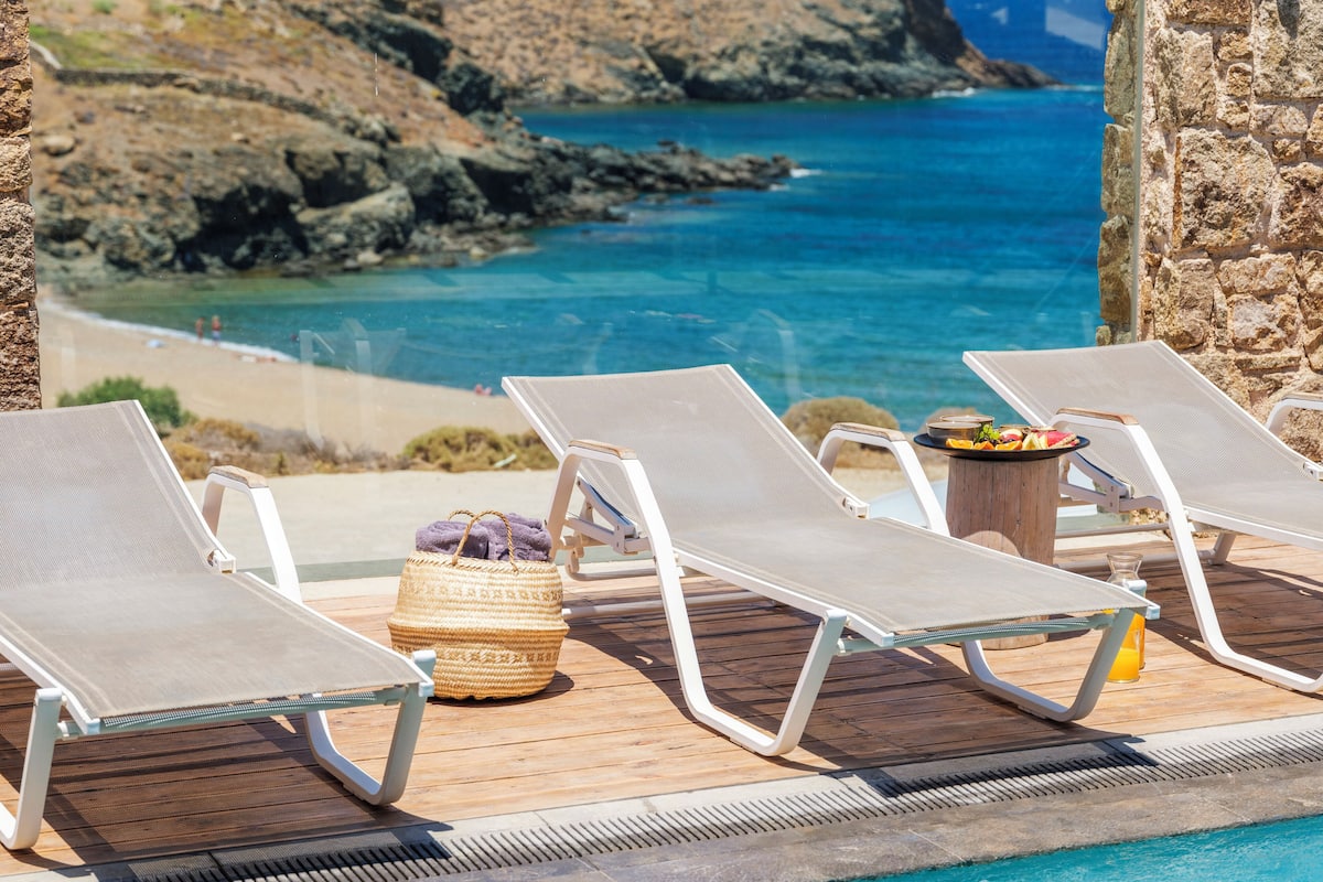 Un área junto a la piscina con sillas de descanso y una mesa con bebidas y aperitivos.