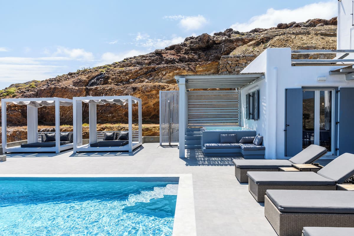 Zona de piscina con sillones de descanso y un jacuzzi, con vistas a una ladera rocosa.