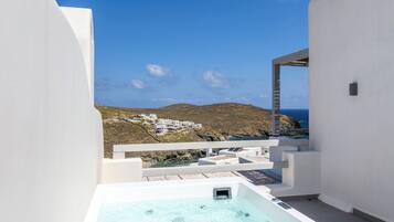 A rooftop terrace with a hot tub, white walls, and a view of a coastal village.