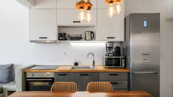 Una cocina moderna con un refrigerador de acero inoxidable, un horno empotrado, un microondas y una cafetera. Hay una mesa de comedor de madera con dos sillas.