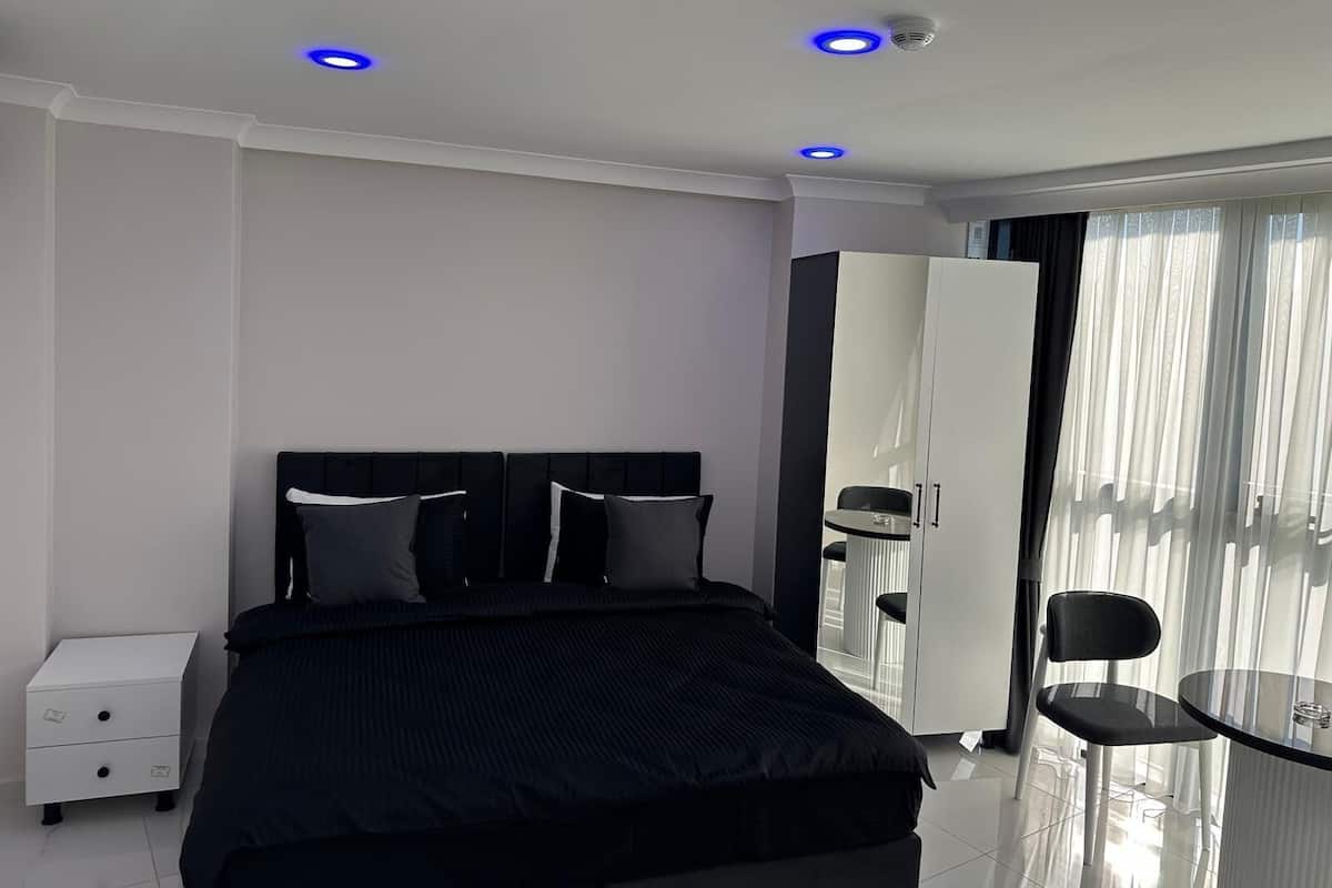 A modern hotel room with a bed, bedside table, wardrobe, and a small round table with a chair.