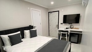 A modern bedroom with a large bed, a desk with a TV, and a door. - Gebze Kent Pansiyon (Gebze)