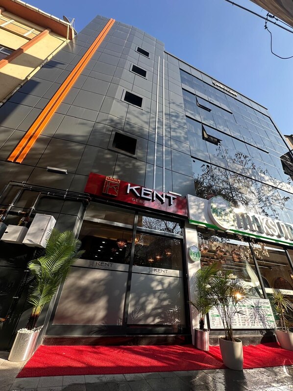 A modern building with a red carpet entrance, a sign for 'KENT GEBZE HOTEL', and a reflection of trees on the glass facade. - Gebze Kent Pansiyon (Gebze)