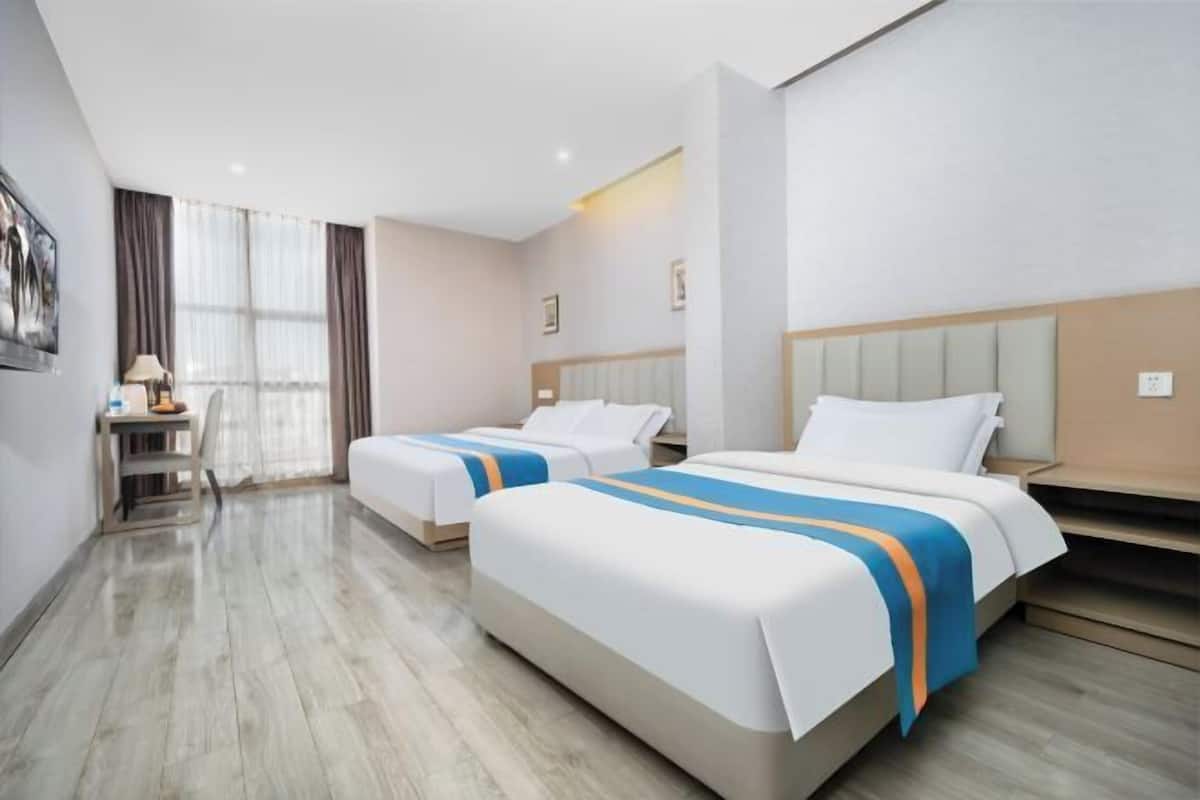 Een hotelkamer met twee bedden, een bureau en een raam met gordijnen.