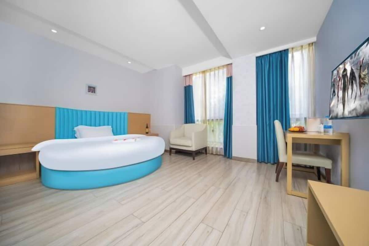 Een moderne hotelkamer met een groot bed, een klein bureau, een stoel en een raam met gordijnen.