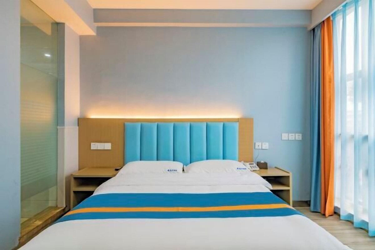 A hotel room with a bed, bedside tables, a nightstand, and a window with curtains.