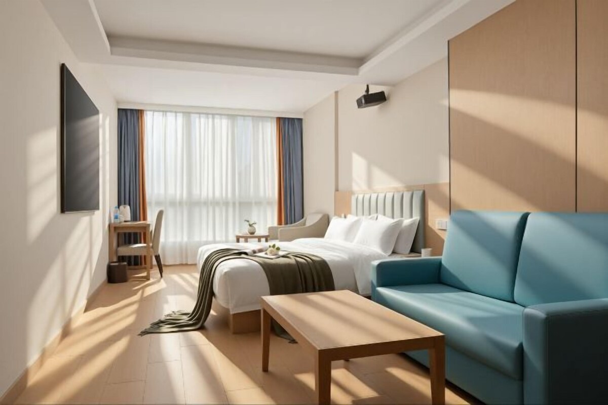 A hotel room with a bed, a blue sofa, a wooden table, and a desk with a chair.