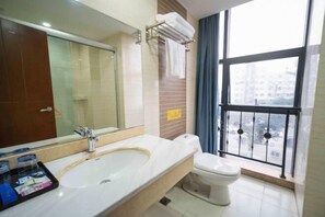 A bathroom with a large sink, mirror, and toilet. There is a window with a view of buildings outside. - Deyang Liansheng Hotel (Deyang)
