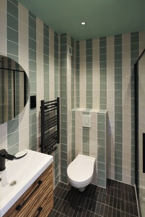 A bathroom with a white sink, a mirror, a black towel rack, a white toilet, and a shower area. - Fernand Cocq Elegant Residence (Brussels)
