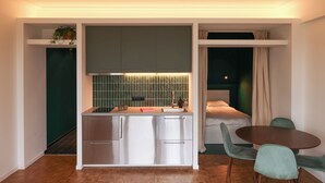 A compact kitchen with a dining area, including a small table and chairs, and a bed with a window. - Fernand Cocq Elegant Residence (Brussels)