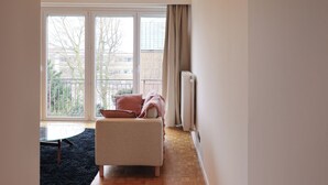 A spacious living room with a large window, a sofa, and a radiator. - Fernand Cocq Elegant Residence (Brussels)