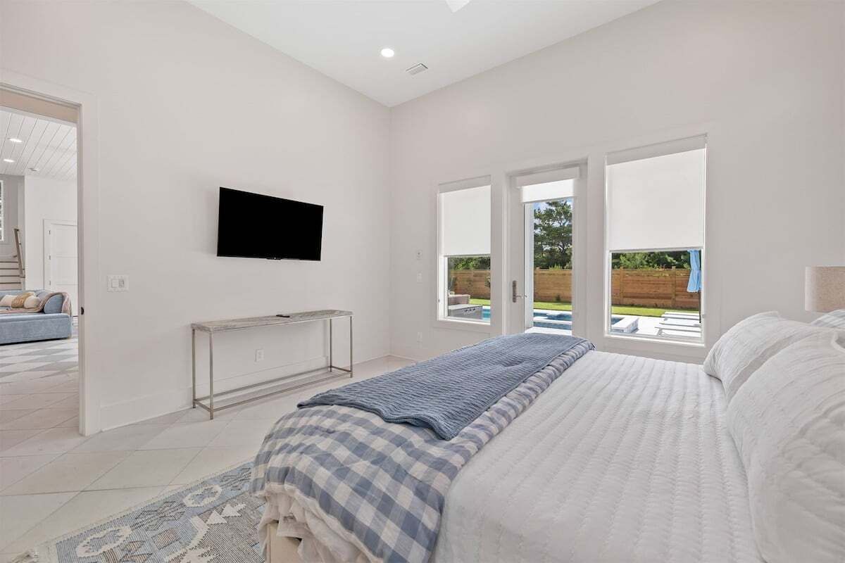 Une chambre avec un lit, un téléviseur fixé au mur et une vue sur une piscine par la fenêtre.