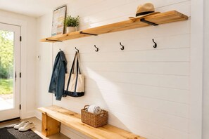 A hallway with a wooden bench, a coat rack with a hat and a jacket, and a basket with towels. - Lake, Spa and Pool Table | Le Gaia (Chertsey)