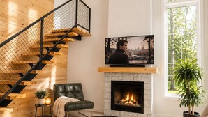 A modern living room with a fireplace, a TV mounted on the wall, a leather chair, and a staircase with a wooden finish. - Lake, Spa and Pool Table | Le Gaia (Chertsey)
