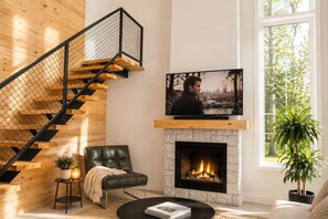 A modern living room with a fireplace, a TV mounted on the wall, a leather chair, and a staircase with a wooden finish. - Lake, Spa and Pool Table | Le Gaia (Chertsey)