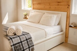 A bed with a wooden headboard, a bedside table with a plant, and a rolled towel on the bed. - Lake, Spa and Pool Table | Le Gaia (Chertsey)