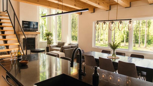 A modern kitchen with a central island, dining area, and a staircase leading to an upper level.