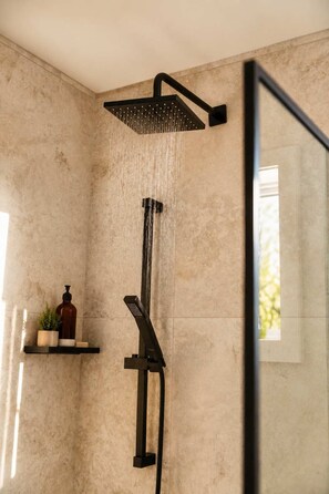 A modern shower with a rain showerhead and a handheld showerhead, mounted on a textured wall.