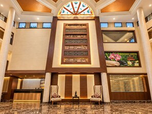 A hotel lobby with a reception desk, two armchairs, a decorative wall with panels, and a massage center advertisement. - The Altruist Katra Hotel (Katra)