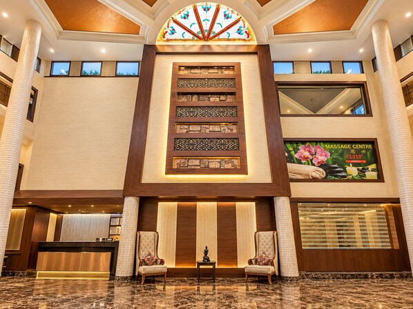 A hotel lobby with a reception desk, two armchairs, a decorative wall with panels, and a massage center advertisement. - The Altruist Katra Hotel (Katra)