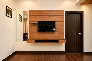 A modern living room with a mounted TV, wooden panel wall, a door, and a mirror. - The Altruist Katra Hotel (Katra)