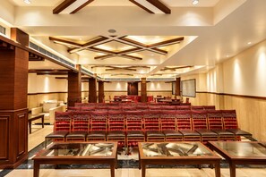 A conference room with tiered seating, wooden paneling, and a modern ceiling design. - The Altruist Katra Hotel (Katra)